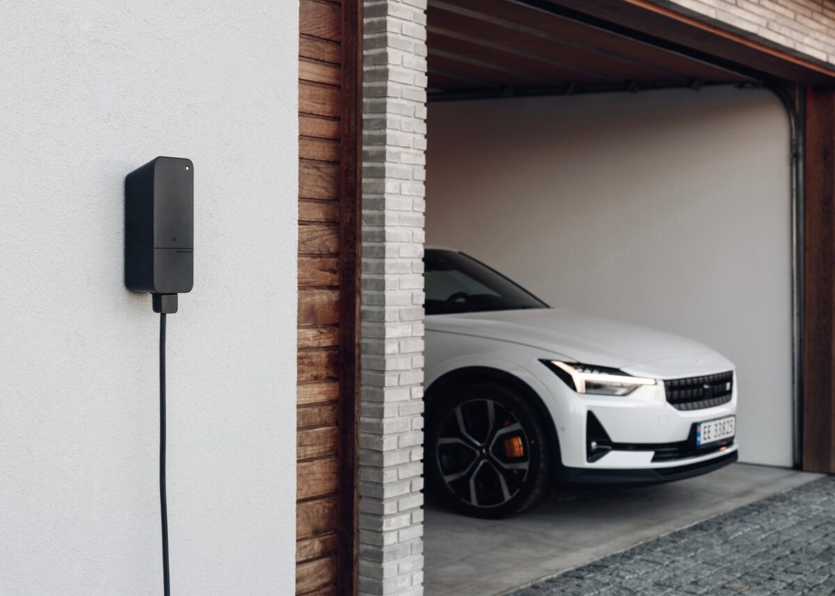 amina C wall-mounted EV charger installed on an exterior house wall beside a modern garage, providing reliable residential electric vehicle charging.