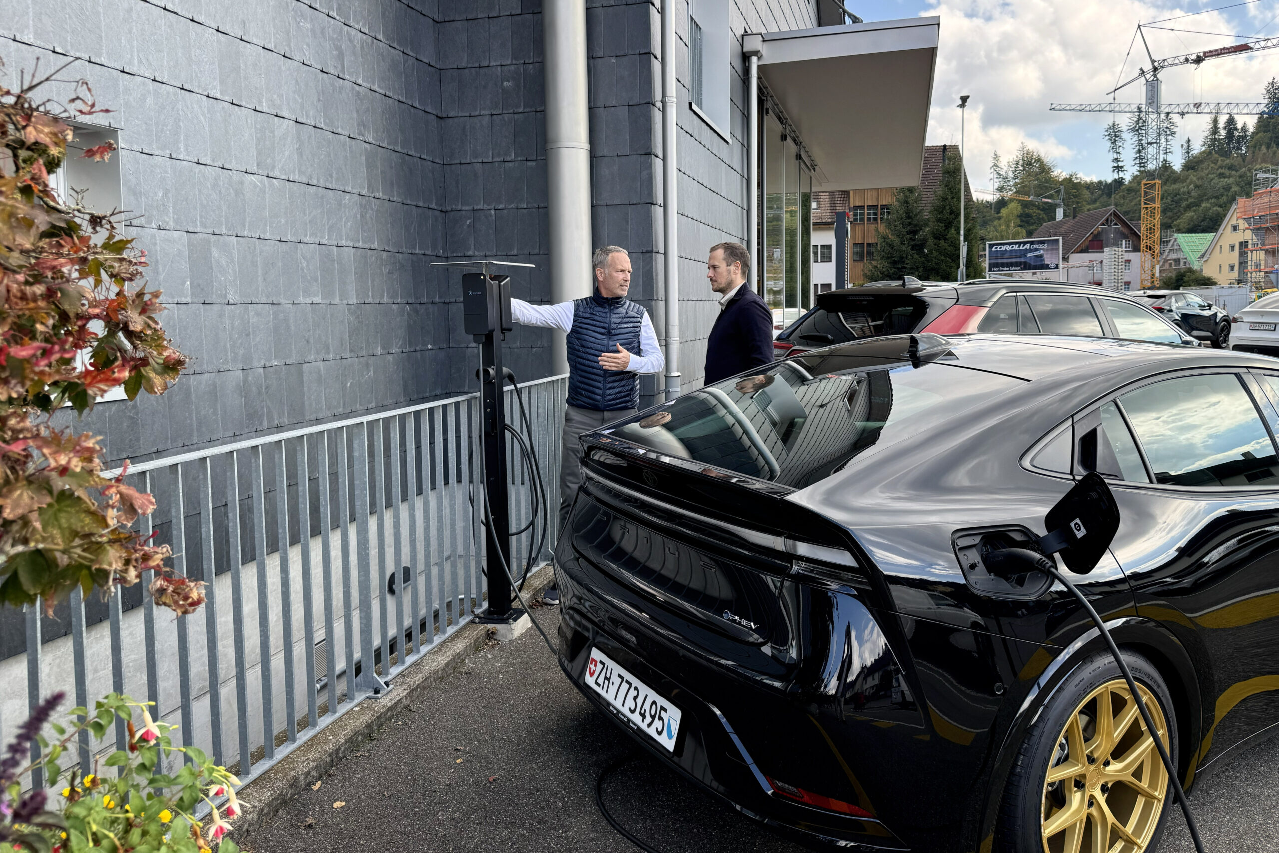 Ronny from Invisia discussing amina charger installation with colleague at Swiss dealership with EV charging in progress