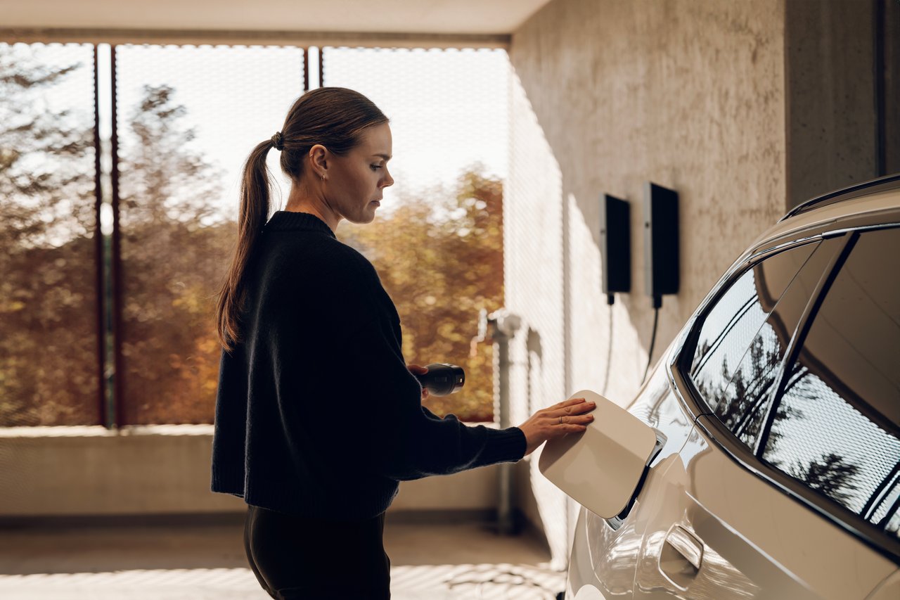Resident charging an electric car in a shared underground parking garage, using a wall-mounted Mode 3 EV charger in a VVE building. Multiple chargers visible in the background, illustrating compliant, coordinated EV charging infrastructure under Dutch building regulations (Bouwbesluit 2024, NEN1010)