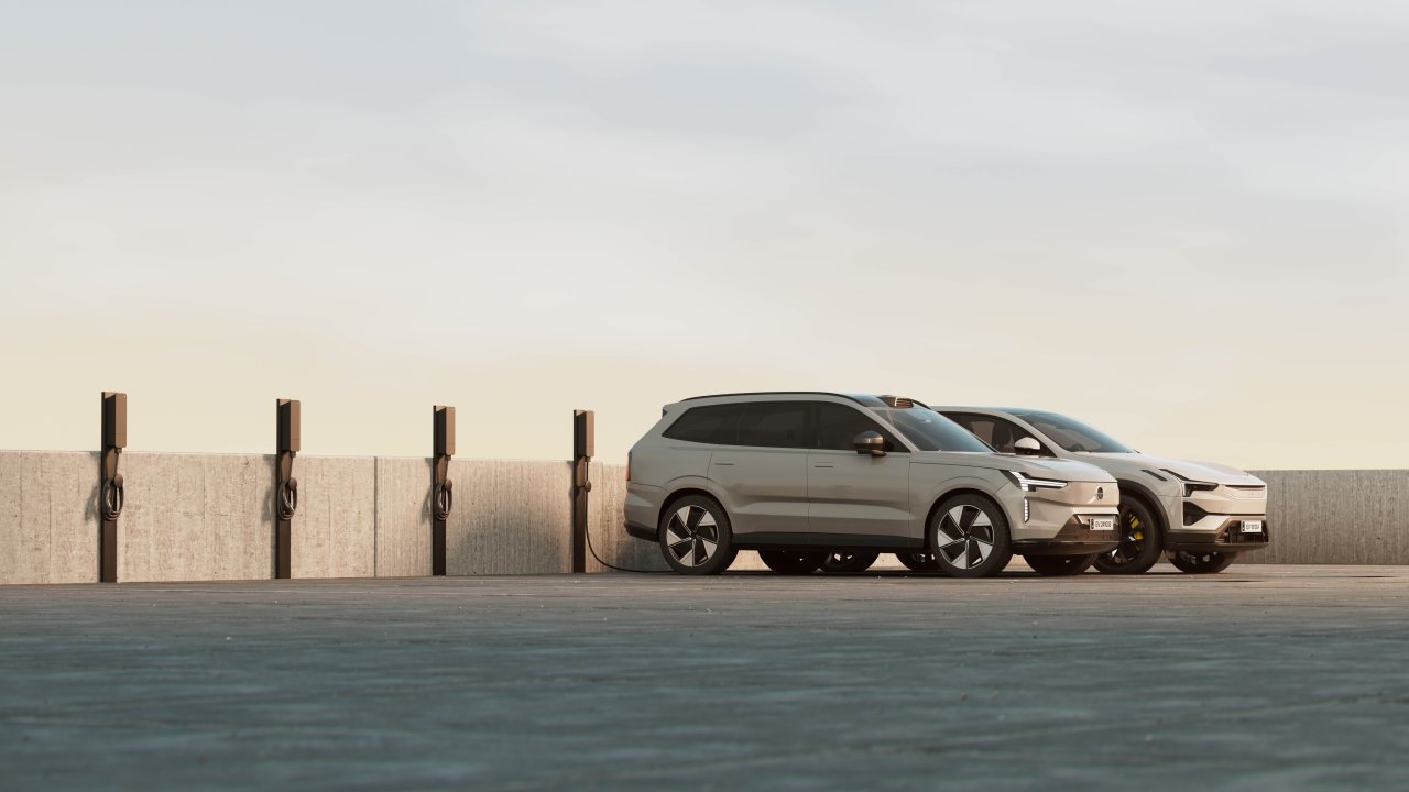 Two electric cars parked in marked bays beside multiple amina M EV charging stations mounted on posts along a commercial building wall, demonstrating scalable shared charging infrastructure for multi-dwelling or workplace environments.